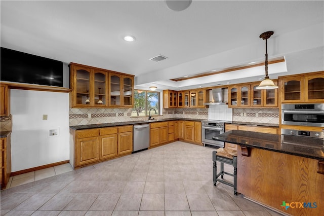 kitchen featuring stainless steel appliances, tasteful backsplash, wall chimney range hood, pendant lighting, and dark stone countertops