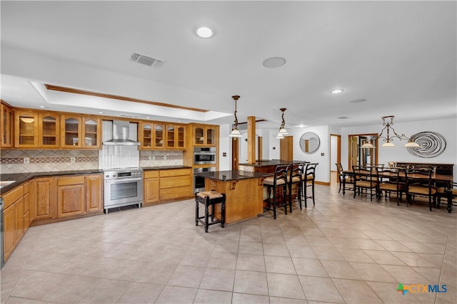 kitchen with tasteful backsplash, stainless steel appliances, wall chimney range hood, hanging light fixtures, and a breakfast bar