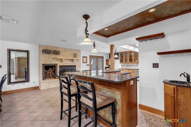 kitchen featuring sink, a breakfast bar area, light tile patterned floors, decorative light fixtures, and a fireplace