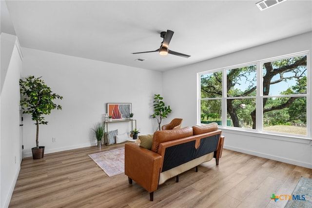 living area with baseboards, light wood-style floors, visible vents, and ceiling fan