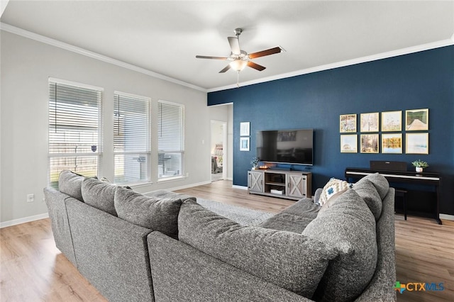 living room featuring wood finished floors, baseboards, ceiling fan, an accent wall, and crown molding