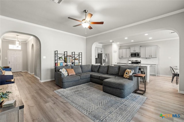 living area featuring arched walkways, light wood finished floors, baseboards, and ceiling fan