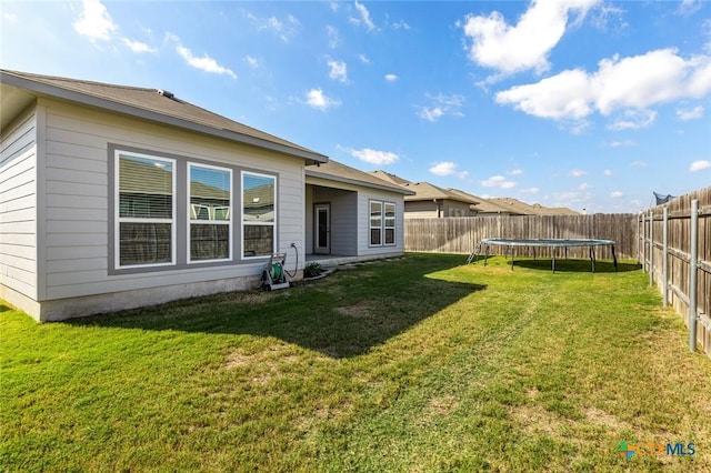 back of house featuring a trampoline, a fenced backyard, and a lawn