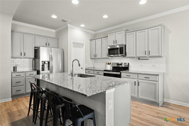 kitchen with light wood finished floors, a breakfast bar, a sink, gray cabinetry, and stainless steel appliances