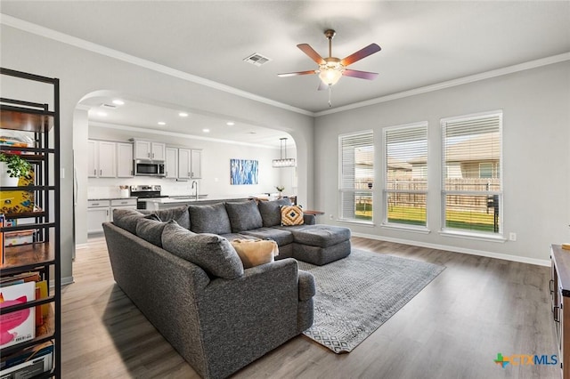 living room with light wood-style flooring, arched walkways, ceiling fan, and ornamental molding