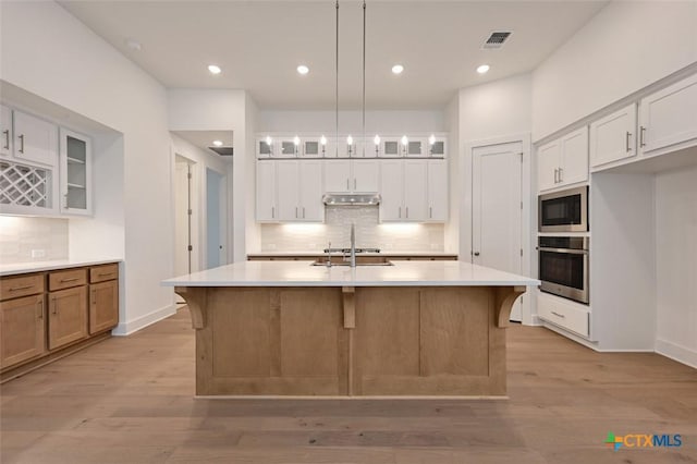 264 Five Mile Creek Way, Kyle, TX 78640 - kitchen featuring stainless steel appliances, under cabinet range hood, tasteful backsplash, glass insert cabinets, and light wood-style flooring