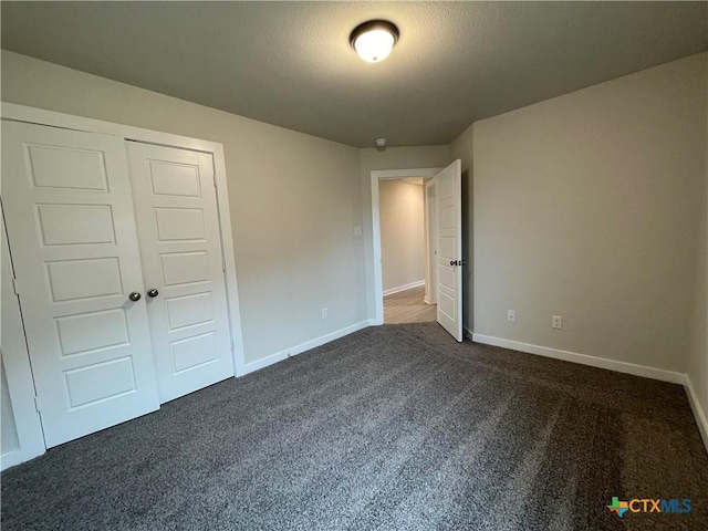 unfurnished bedroom with a textured ceiling, a closet, and dark colored carpet