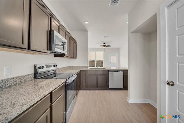 kitchen featuring sink, dark brown cabinetry, light stone counters, stainless steel appliances, and light hardwood / wood-style floors