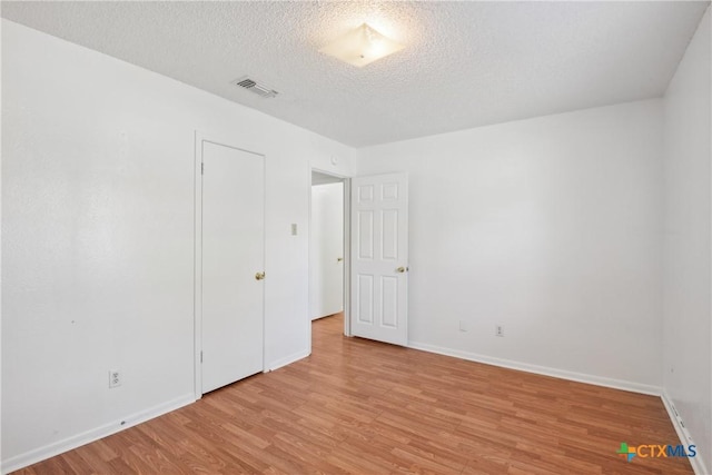 empty room featuring visible vents, baseboards, a textured ceiling, and light wood-style flooring