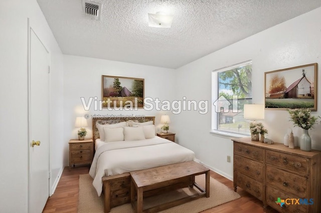 bedroom with light wood finished floors, visible vents, a textured ceiling, and baseboards