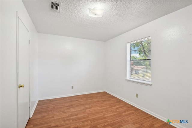 spare room with visible vents, a textured ceiling, light wood-type flooring, and baseboards