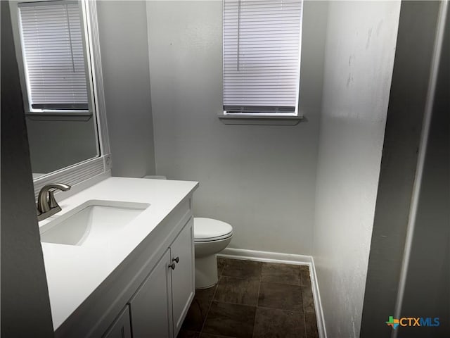 half bath featuring baseboards, toilet, and vanity