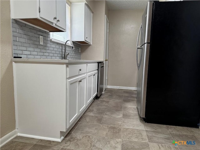 kitchen with freestanding refrigerator, a sink, light countertops, white cabinetry, and backsplash