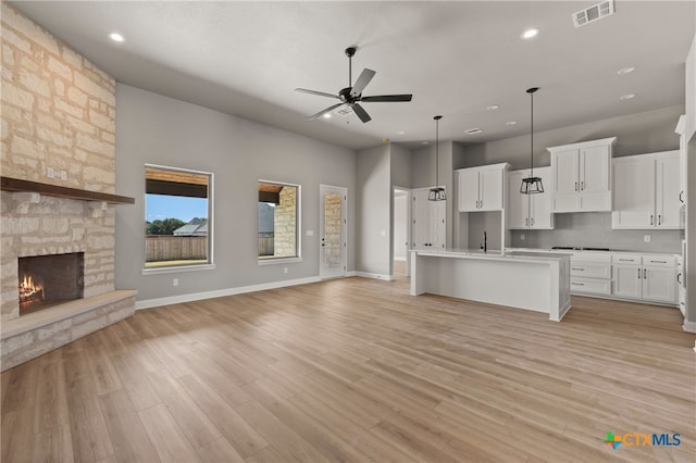 kitchen with a fireplace, ceiling fan, a center island with sink, white cabinets, and light hardwood / wood-style floors