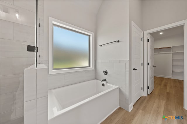 bathroom featuring wood-type flooring, a tub to relax in, and tile walls