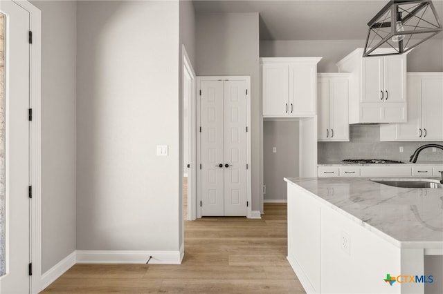 kitchen with light stone countertops, sink, white cabinets, and pendant lighting