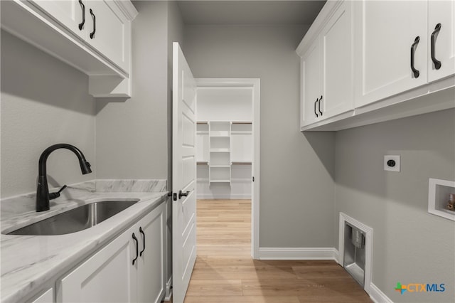 clothes washing area with electric dryer hookup, sink, cabinets, and light hardwood / wood-style flooring