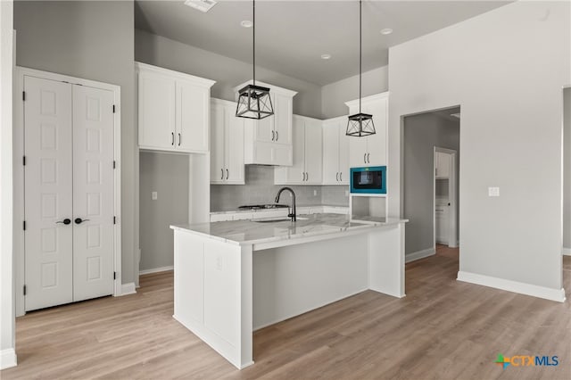 kitchen featuring a kitchen island with sink, white cabinets, hanging light fixtures, light hardwood / wood-style flooring, and black microwave