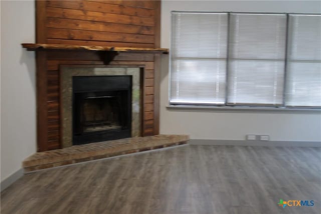 unfurnished living room featuring a brick fireplace, baseboards, and wood finished floors