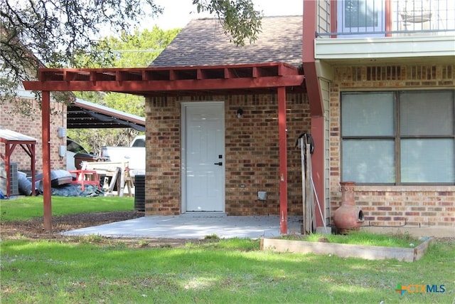 doorway to property with a yard, brick siding, and a shingled roof