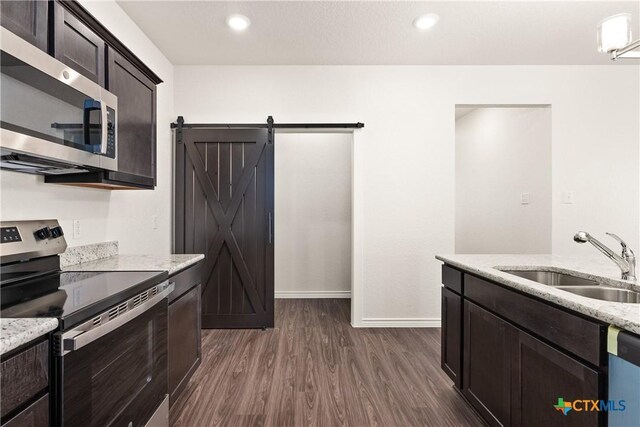 kitchen with a sink, stainless steel appliances, a barn door, dark brown cabinets, and dark wood-style flooring