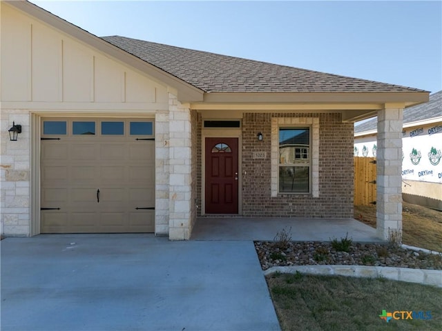 property entrance with a garage, board and batten siding, concrete driveway, and a shingled roof