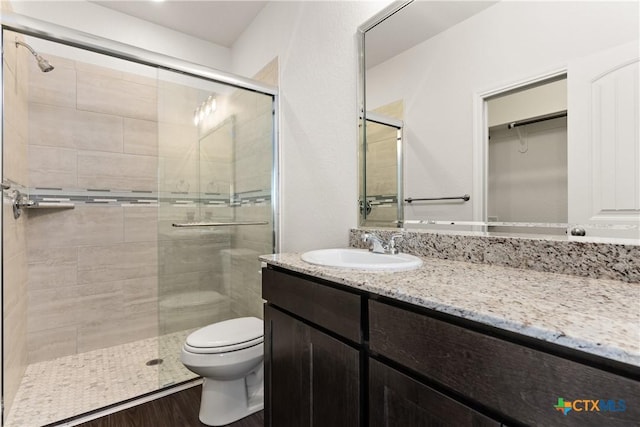 bathroom with a shower stall, toilet, vanity, and wood finished floors