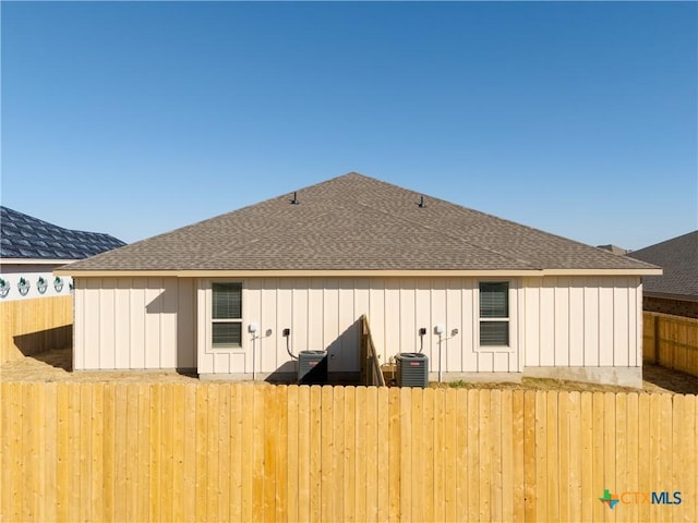 back of house featuring board and batten siding, roof with shingles, and fence