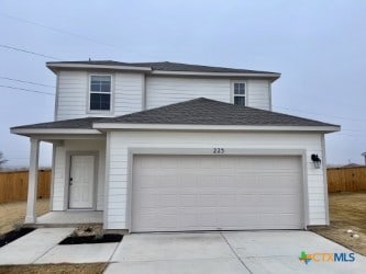 traditional-style house with an attached garage, concrete driveway, and fence