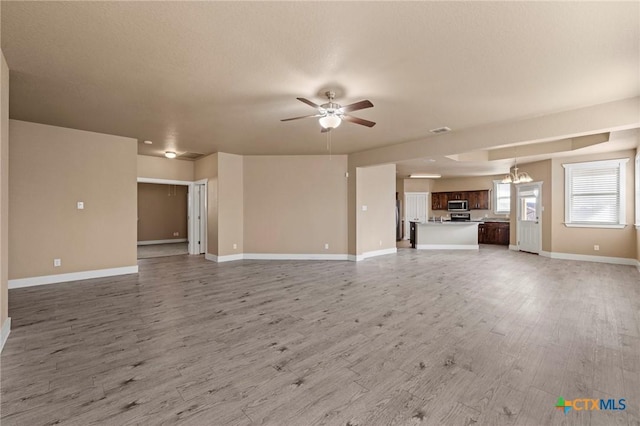 unfurnished living room with visible vents, light wood-style flooring, baseboards, and ceiling fan with notable chandelier