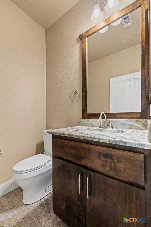 bathroom featuring visible vents, a textured wall, vanity, and toilet