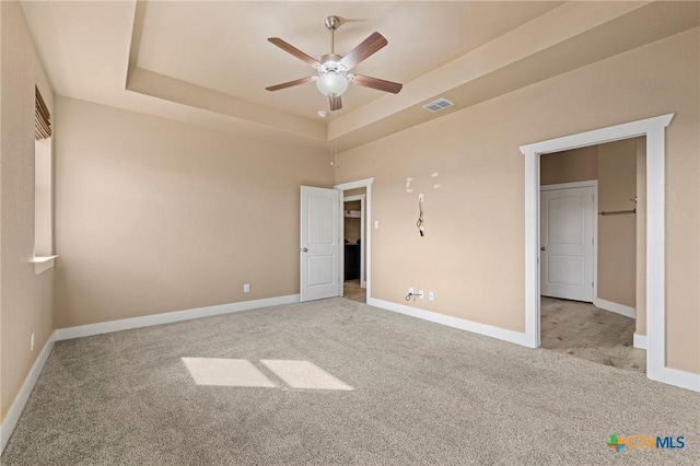 unfurnished bedroom featuring visible vents, baseboards, a ceiling fan, a tray ceiling, and carpet floors