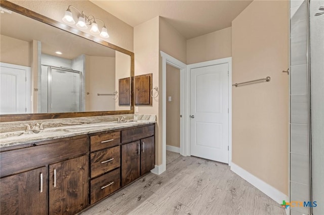 bathroom with double vanity, a stall shower, a sink, and wood finished floors