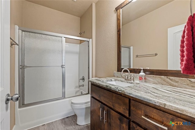 full bath featuring toilet, shower / bath combination with glass door, wood finished floors, and vanity