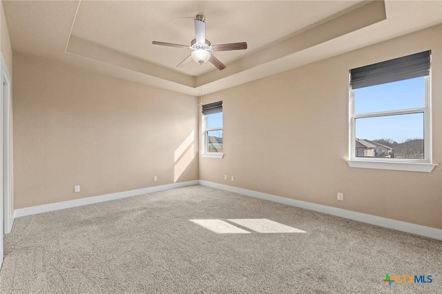 carpeted spare room featuring a tray ceiling, ceiling fan, and baseboards