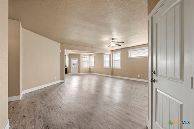 interior space with a ceiling fan, a textured ceiling, baseboards, and wood finished floors