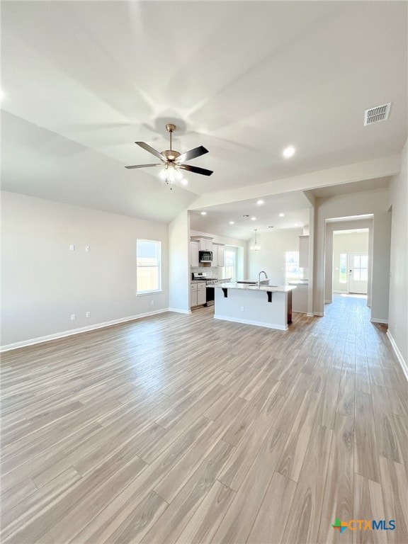 unfurnished living room featuring sink, vaulted ceiling, ceiling fan, and light hardwood / wood-style flooring