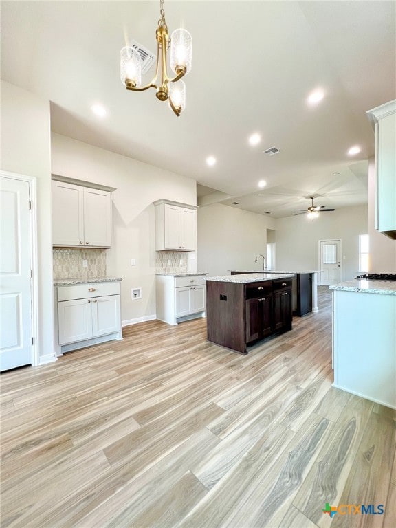 kitchen with white cabinetry, backsplash, light hardwood / wood-style floors, and ceiling fan with notable chandelier