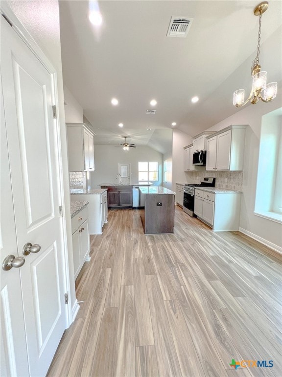 kitchen featuring light hardwood / wood-style floors, decorative backsplash, appliances with stainless steel finishes, white cabinets, and vaulted ceiling