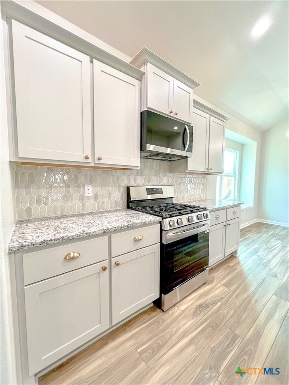 kitchen with stainless steel appliances, light stone counters, light hardwood / wood-style floors, and tasteful backsplash