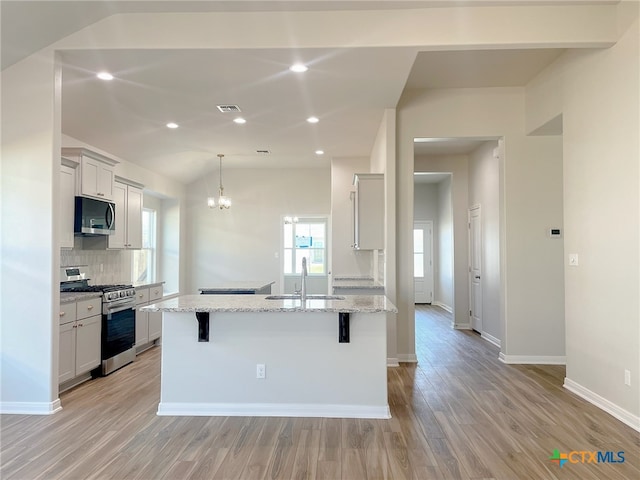 kitchen with light stone counters, a breakfast bar area, a kitchen island with sink, light wood-type flooring, and appliances with stainless steel finishes