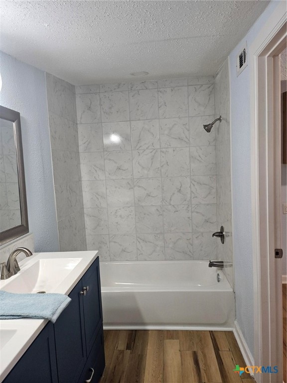 bathroom featuring vanity, wood-type flooring, a textured ceiling, and tiled shower / bath