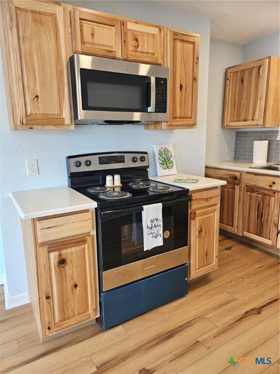 kitchen featuring sink, light wood-type flooring, decorative backsplash, and electric range