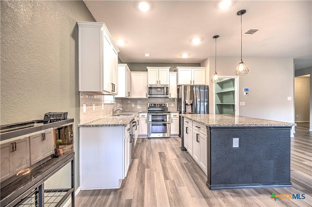 kitchen with white cabinets, a center island, hanging light fixtures, and appliances with stainless steel finishes