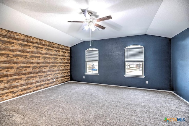 empty room featuring ceiling fan, wood walls, lofted ceiling, and carpet flooring