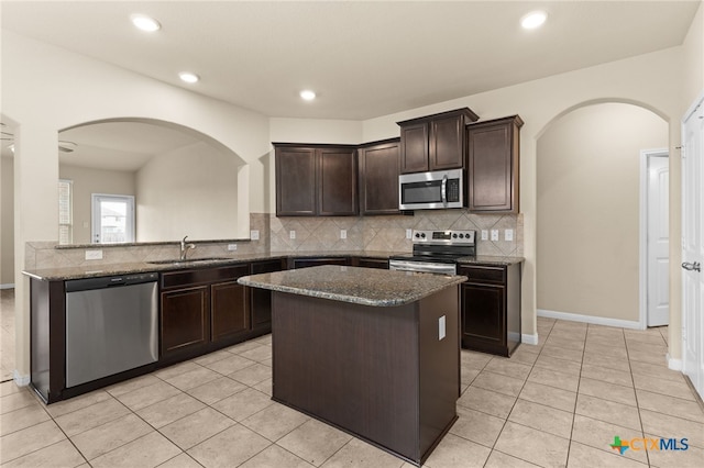 3411 Aubree Katherine Dr, Killeen, TX 76542 - kitchen featuring appliances with stainless steel finishes, arched walkways, dark brown cabinetry, dark stone countertops, and backsplash