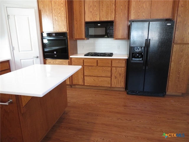 kitchen with dark hardwood / wood-style flooring, decorative backsplash, a center island, and black appliances