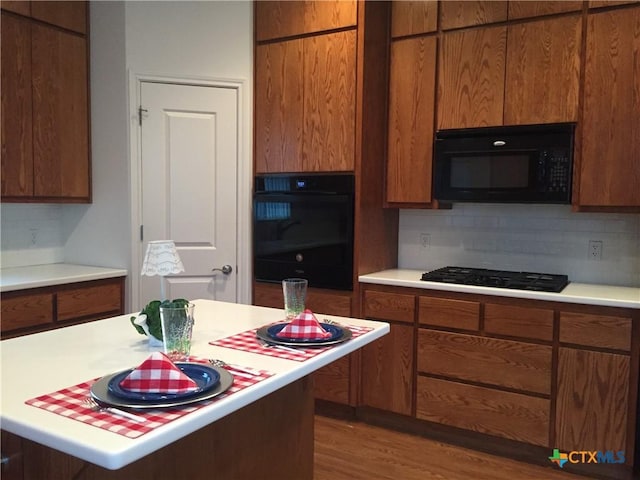 kitchen with black appliances, light wood-type flooring, and decorative backsplash