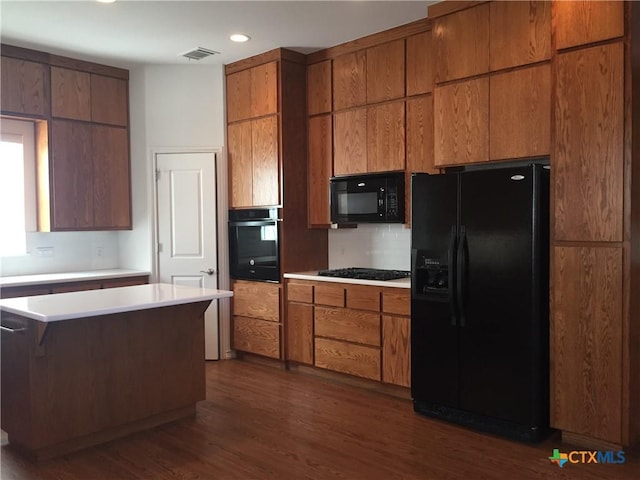 kitchen with black appliances, a center island, dark wood-type flooring, a kitchen breakfast bar, and backsplash