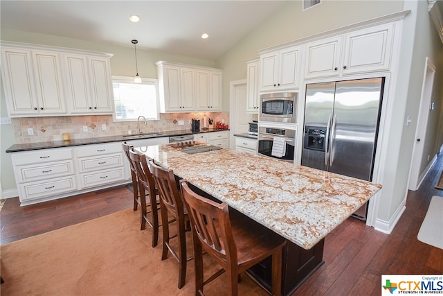 kitchen with a center island, built in appliances, sink, dark hardwood / wood-style floors, and pendant lighting